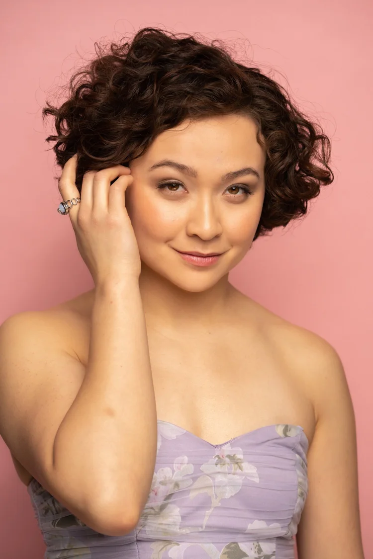 Soft formal makeup in a lilac-dress studio portrait.